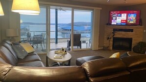 Ein Wohnzimmer mit einer Ledersofa, einem Kamin, einem Fernseher und Blick auf ein Gewässer durch große Schiebetüren.