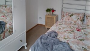 Et soveværelse med en seng, et skab, et natbord med en plante og et spejl.
