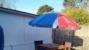 En træterrasse med et bord og stole under en stor parasol.