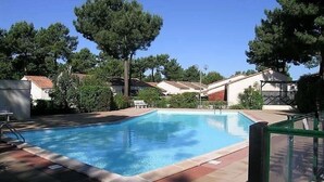 A rectangular swimming pool with a tiled deck, surrounded by trees and residential buildings. - La Palmyre - Le HAMEAU de TALARIS - TERRACED HOUSE - SHARED POOL (LA PALMYRE)