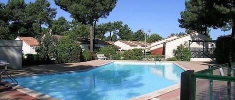 Una piscina rectangular con un borde empedrado, rodeada de árboles y edificios residenciales.