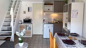 A compact kitchen with a microwave, refrigerator, and small dining area with a table set for two. - La Palmyre - Le HAMEAU de TALARIS - TERRACED HOUSE - SHARED POOL (LA PALMYRE)