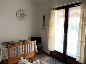 A room with a dining table set for two, a wooden chair, a television, and a window with curtains.
