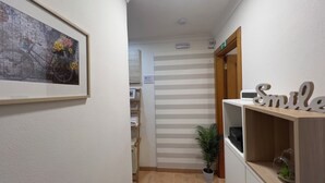Un couloir aux murs rayés, un tableau encadré, une décoration représentant un sourire, une plante en pot et une étagère avec une horloge.