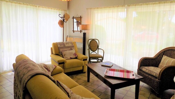 Un salon avec un canapé jaune, un fauteuil en osier, une table basse et une lampe.