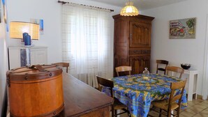 Un coin repas avec une table en bois, des chaises, une vieille malle, une lampe, un meuble et un tableau accroché au mur.