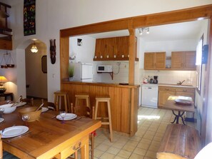 Une cuisine avec des meubles de rangement en bois, un coin repas avec une table et des chaises en bois, et un petit îlot central avec des tabourets.