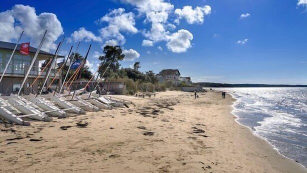 Una playa con barcos alineados, un edificio con una bandera y un cielo despejado.
