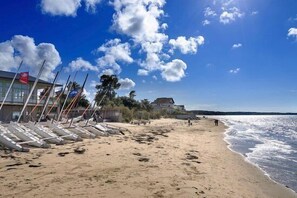 A beach with boats lined up, a building with a flag, and a clear sky. - La Tremblade – DISCOVER this MOBILE HOME on a PRIVATE PLOT (LA TREMBLADE)