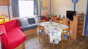 Una habitación compacta con un sofá rojo, una mesa de comedor con sillas, un televisor y un ventilador de techo.