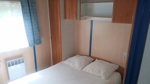 Una cama individual con cabecera de madera, una ventana con cortina y un calefactor fijado a la pared.