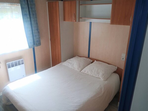 Una cama individual con cabecera de madera, una ventana con cortina y un calefactor fijado a la pared.