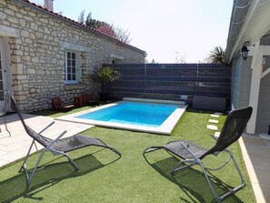 Une piscine avec deux chaises longues, un mur en pierre et une zone délimitée par une clôture.