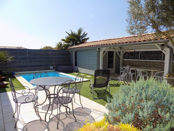 Un jardin avec une piscine, du mobilier de jardin et un espace barbecue couvert.