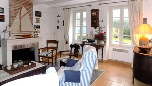 A cozy living room with a fireplace, a sailboat model, and a dining area with striped chairs. - Les Mathes La Palmyre - CHARMING CHARENTAISE HOUSE - PEACEFUL - COUNTRYSIDE (LES MATHES)