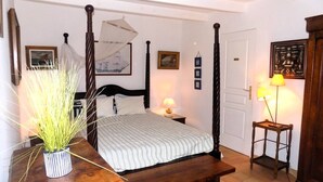 A four-poster bed with a striped bedspread, a bedside table with a lamp, and a potted plant. - Les Mathes La Palmyre - CHARMING CHARENTAISE HOUSE - PEACEFUL - COUNTRYSIDE (LES MATHES)