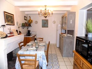 Ein Essbereich mit Tisch für vier Personen, einer Chandelüster und einer Küchenzeile mit Mikrowelle und Kühlschrank.