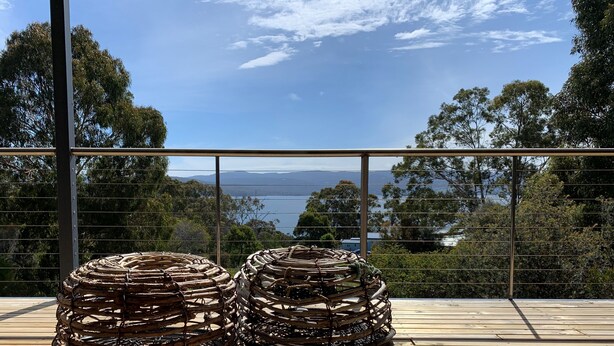 A wooden deck with two large, coiled metal structures, overlooking a scenic landscape with trees and a body of water.