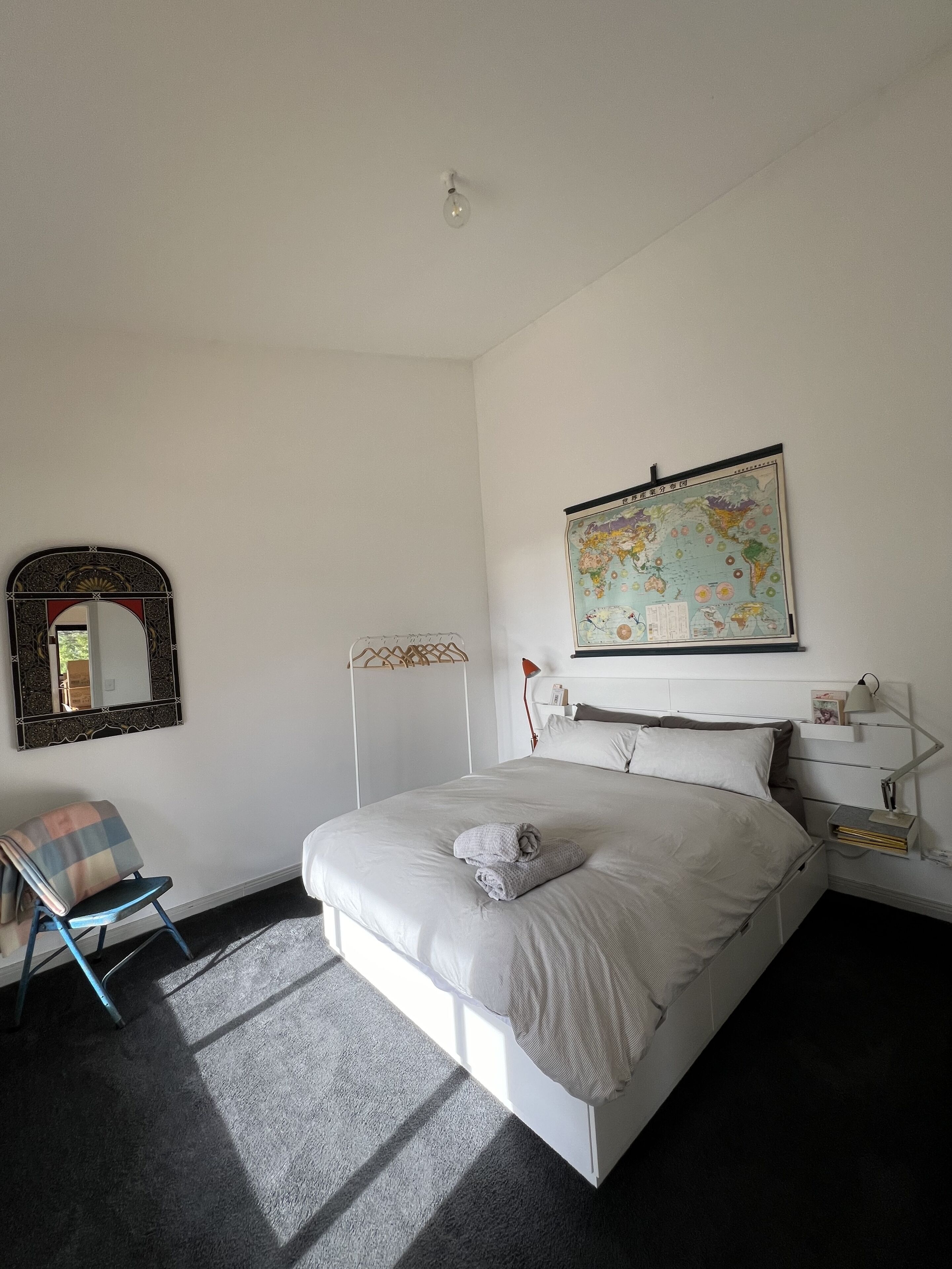 Une chambre à coucher avec un lit, une carte accrochée au mur, un miroir, une chaise et une table de chevet avec une lampe.