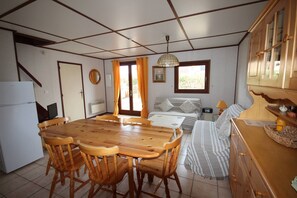 A compact room with a dining table, chairs, a bed, a small table with a lamp, and a wardrobe.