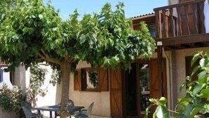 Eine Terrasse mit Tisch und Stühlen, ein Baum spendet Schatten, und ein Holzzaun.