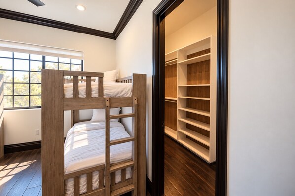 A bunk bed with a wooden ladder, a walk-in closet with shelves, and a window with a view of trees.