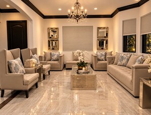 Amplia sala de estar con candelabro, sofás, una mesa de centro y espejos decorativos.