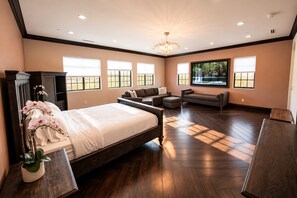 Un dormitorio amplio con una cama grande, una zona de estar con sofás y vistas a zonas verdes por las ventanas.