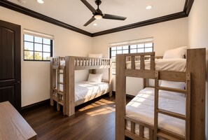 Una habitación con literas, ventilador de techo y ventanas amplias.