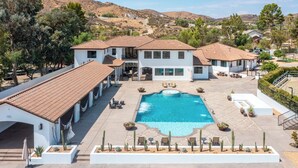 A two-story house with a swimming pool, surrounded by cacti and trees.