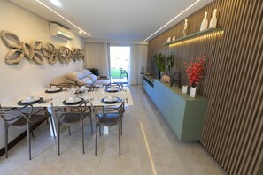 A modern dining area with a long table set for four, a sofa, and a decorative wall piece. - MERIDIONAL FLAT CARNEIROS  (Tamandare)