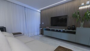 Un salon moderne avec un grand téléviseur à écran plat, un canapé, une table basse et une plante.