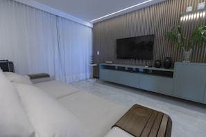 Uma sala de estar moderna com uma televisão de tela plana grande, um sofá, uma mesa de centro e uma planta.
