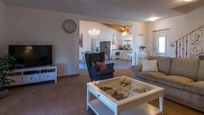 Een moderne woonkamer met een flatscreen televisie, een glazen salontafel, een bank en een eethoek met een kroonluchter.