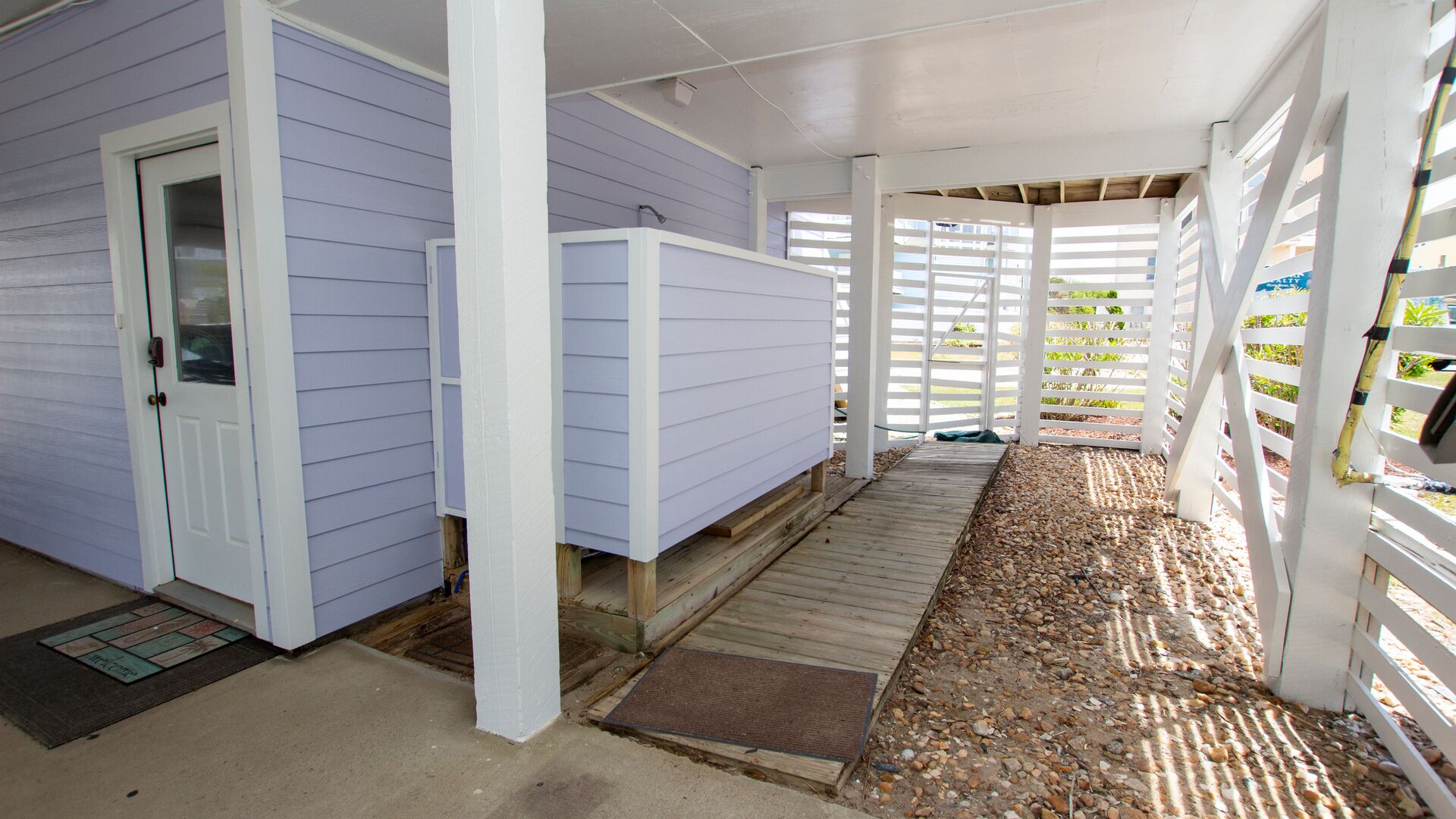 A covered porch with a wooden deck, a door, and a white fence.