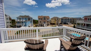 Un balcone con due poltrone Adirondack, una piscina e vista su una comunità sulla spiaggia con edifici a più piani.