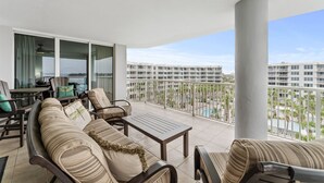 A balcony with a sofa, chairs, and a table, overlooking a pool and buildings. - Destin West Osprey 604  ~ 3BR w/ Bay & Lazy River Views! (Fort Walton Beach)