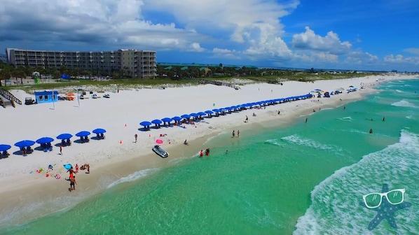 Relax on the sandy beach, surrounded by clear waters and shaded by blue umbrellas.