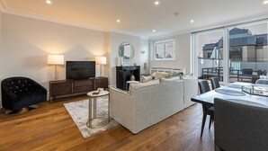 Ett modernt vardagsrum med en soffa, en tv och en matplats, med ett stort fönster och utsikt över stadsbilden.