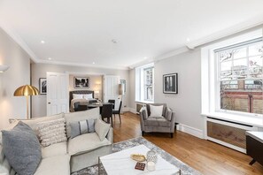 A spacious living room with a sofa, armchair, and coffee table. There is a dining area with chairs and a table, and a kitchen in the background. - Stylish apartment with terrace in Mayfair (London)