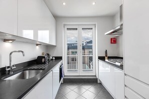 A modern kitchen with a black countertop, stainless steel sink, and white cabinets. - Stylish apartment with terrace in Mayfair (London)