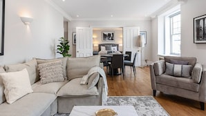 Ein modernes Wohnzimmer mit Sofa, Sessel und Couchtisch. Im Hintergrund ist ein Essbereich mit Stühlen und Tisch zu sehen.