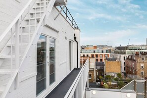 A white building with a balcony, large windows, and a view of surrounding buildings. - Stylish apartment with terrace in Mayfair (London)