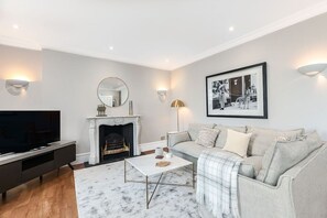 A living room with a fireplace, a sofa, a coffee table, and a television. - Stylish apartment with terrace in Mayfair (London)