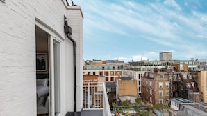Ein Balkon mit einer weißen Backsteinwand, einer Glastür und Blick auf die Stadtlandschaft.