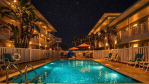 Un espace piscine aménagé pour la nuit, offrant une vue dégagée sur le ciel, et entouré de palmiers et de chaises longues.