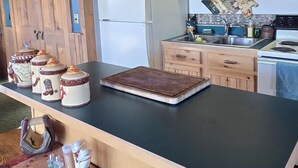 A rustic kitchen with wooden cabinets, a black countertop, and a large window above the sink. - Stargazer Bunkhouse- cozy cabin, basecamp for adventures in Yellowstone and beyond (Meeteetse)