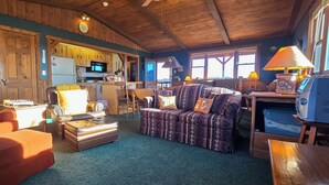 A cozy living room with a fireplace, comfortable seating, and a view of the kitchen. - Stargazer Bunkhouse- cozy cabin, basecamp for adventures in Yellowstone and beyond (Meeteetse)