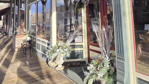 A covered outdoor area with a wooden deck, large windows, and hanging signs. - Stargazer Bunkhouse- cozy cabin, basecamp for adventures in Yellowstone and beyond (Meeteetse)