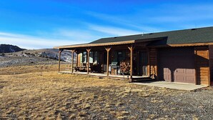A log cabin with a porch and a garage. - Stargazer Bunkhouse- cozy cabin, basecamp for adventures in Yellowstone and beyond (Meeteetse)